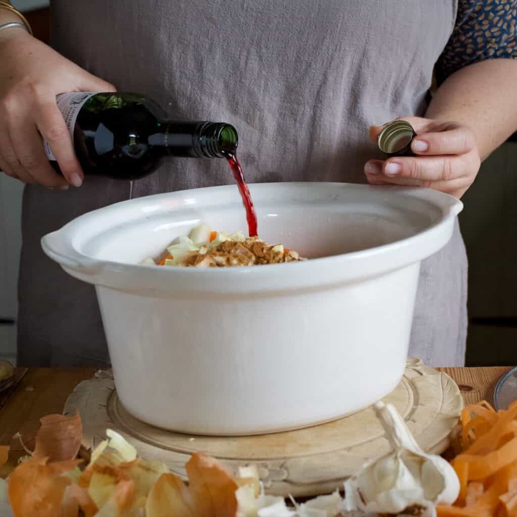 Womans pouring red wine from a glass bottle into a white slow cooker bowl