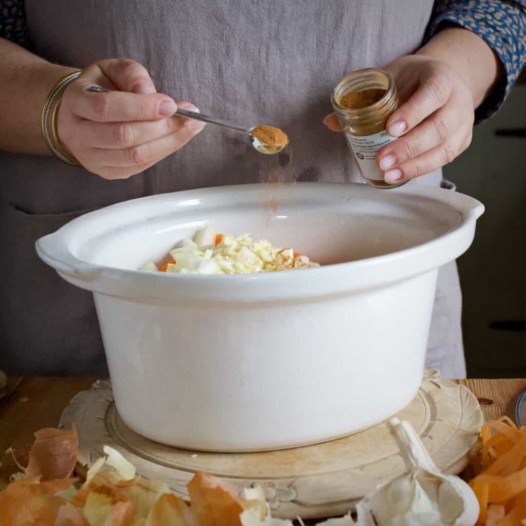 Woman measuring spices from a small glass jar into a white slow cooker