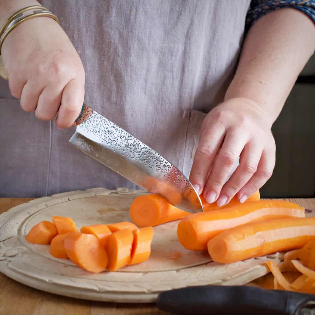 Woamns slicing carrots on a wooden kitchen counter