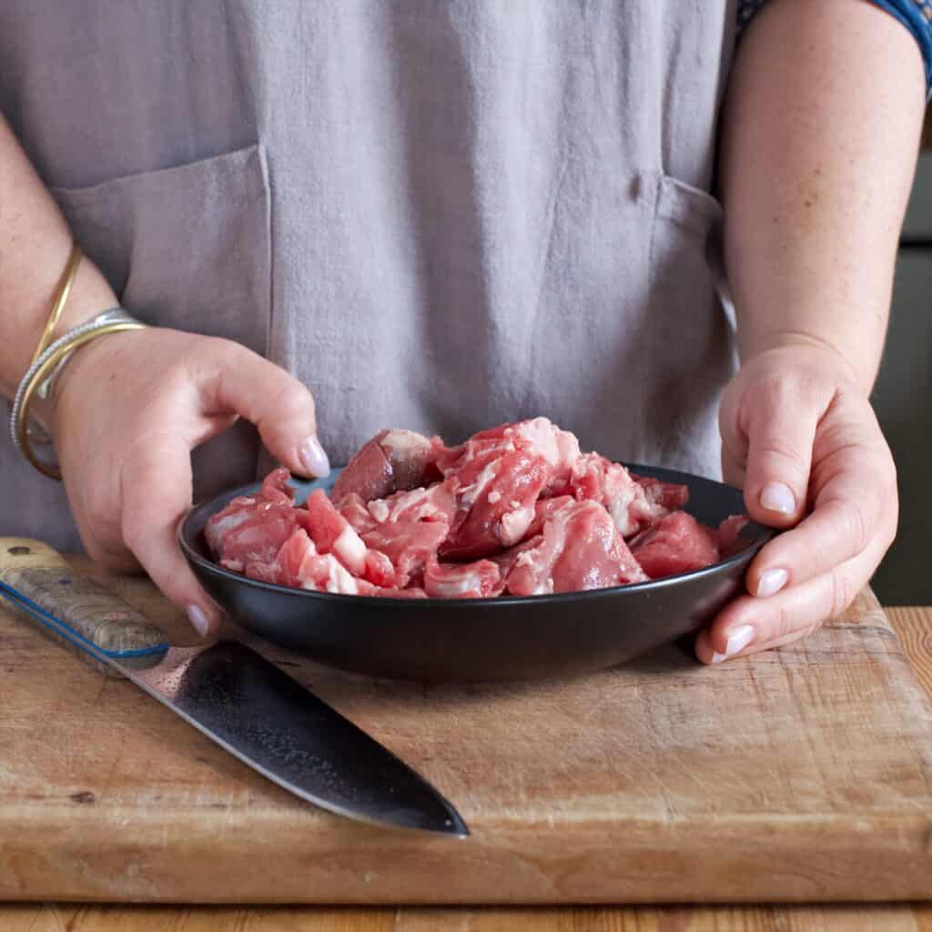 Womans hands holding a black bowl filled with pieces of raw mutton