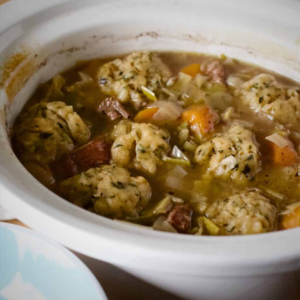 Cooked mutton stew with large dumplings inside a white slow cooker bowl