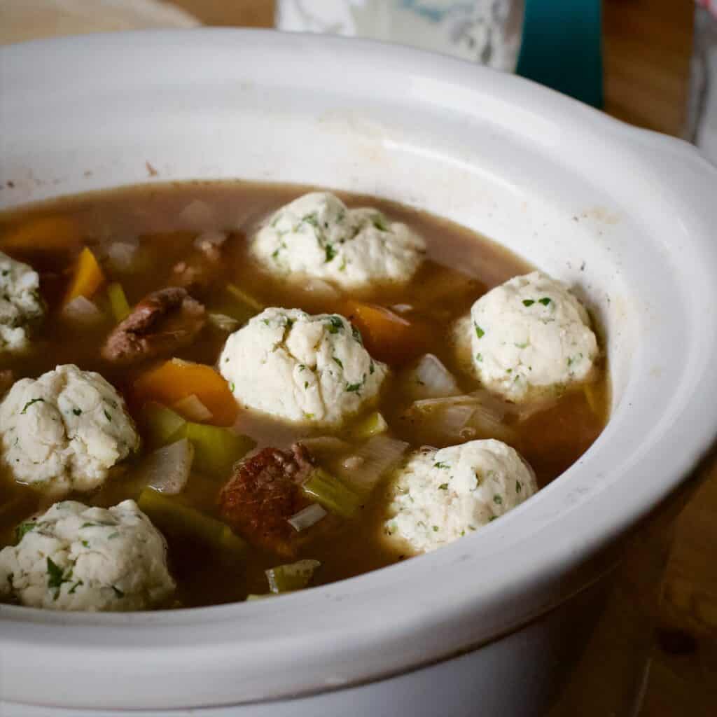 Mutton stew cooking inside a white slow cooker bowl topped with dumplings ready to cook