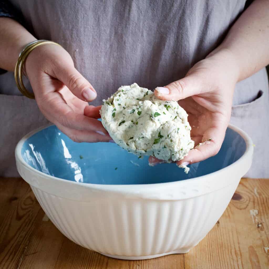 Womans holding a lump of freshly made suet dumpling dough over a blue and white mixing bowl