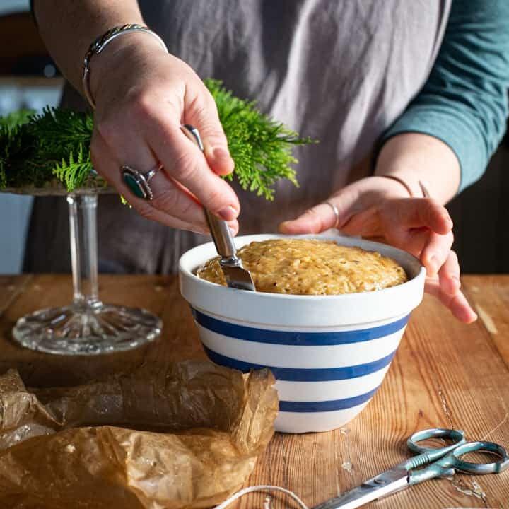 Woman’s hands sliding a knife around a blue and white striped pudding basin to loosen the suet pudding inside