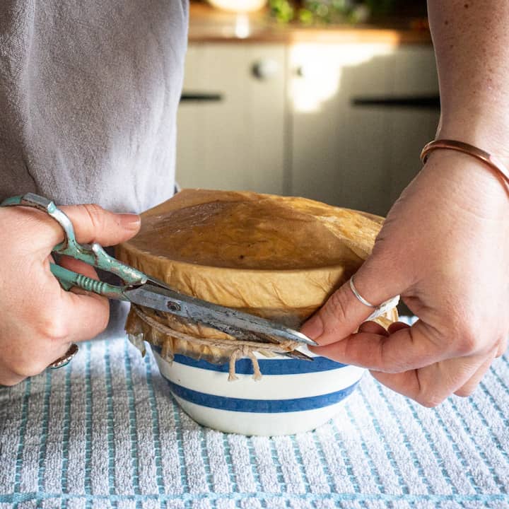 Woman’s hands cutting the string from a pudding basin covered in brown baking paper