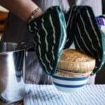 Woman’s hands in green stripy oven gloves placing a hot steamed pudding onto a tea towel