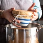Womans hand placing a stripey pudding basin into a large silver saucepan