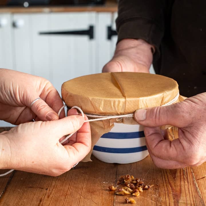 Hands of a man and a woman tying white string around the rim of a blue and white pudding basin to hold on the baking paper lid