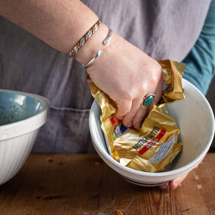 Woman’s hands greasing a white pudding basin with a gold and red butter wrapper