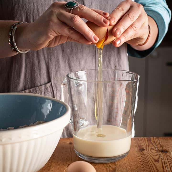 Womans hands cracking an egg into a glass jug part filled with milk