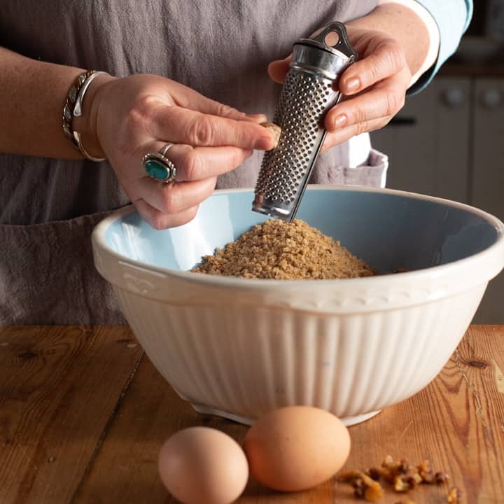 Womans hands grating a nutmeg on a silver grater over a large blue and white mixing bowl