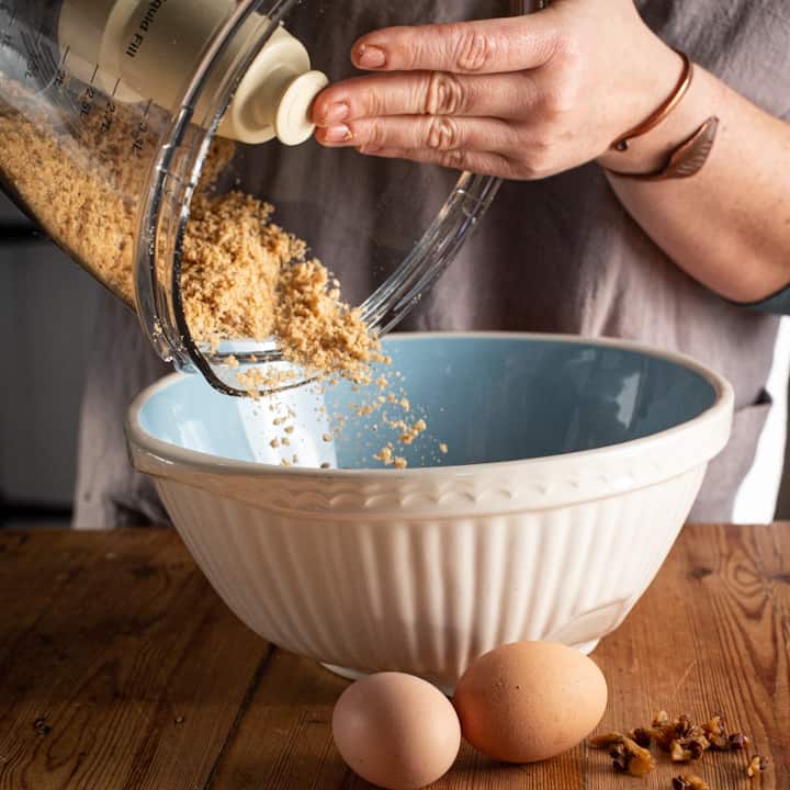 Woman shaking freshly ground breadcrumbs from a food processor bowl into a blue and white mixing bowl