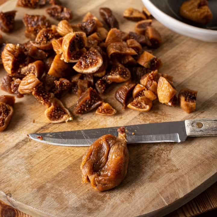 Wooden chopping board with several pieces of diced dried fig and a small sharp knife