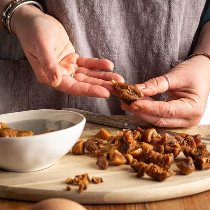 Woman holding a dried fig to show the stalk that needs removing before using for baking