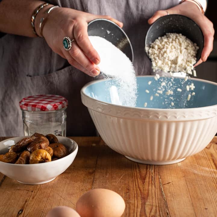 Woman’s hands pouring sugar and suet from 2 brown bowls into a large blue and white mixing bowl