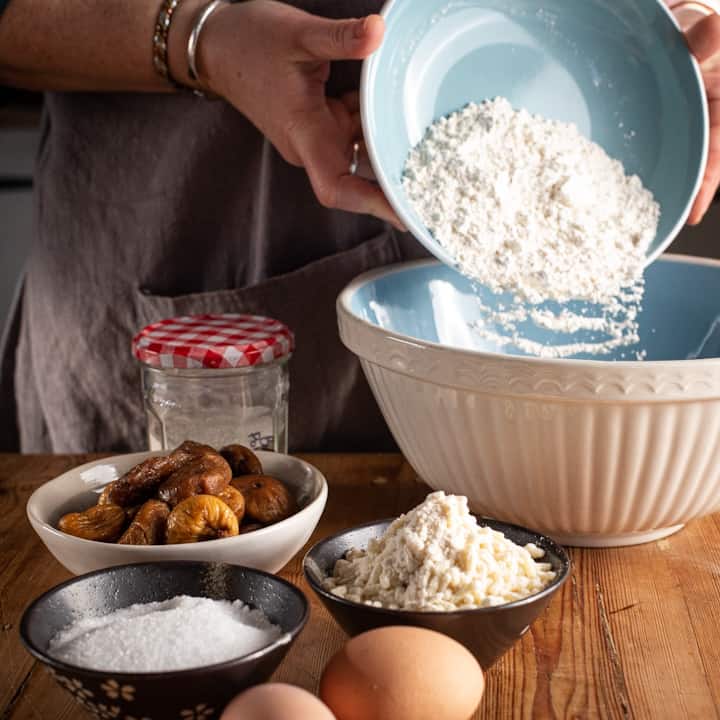 Woman’s hands shaking the flour from a pale blue bowl into a large white mixing bowl