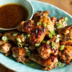 pale blue plate of crispy brown chicken wings with a small bowl of brown dipping sauce