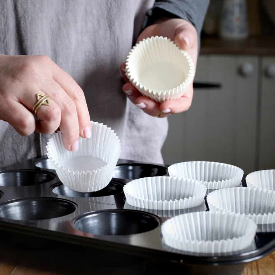 Woman hands placing white paper muffin cases into a black muffin tray