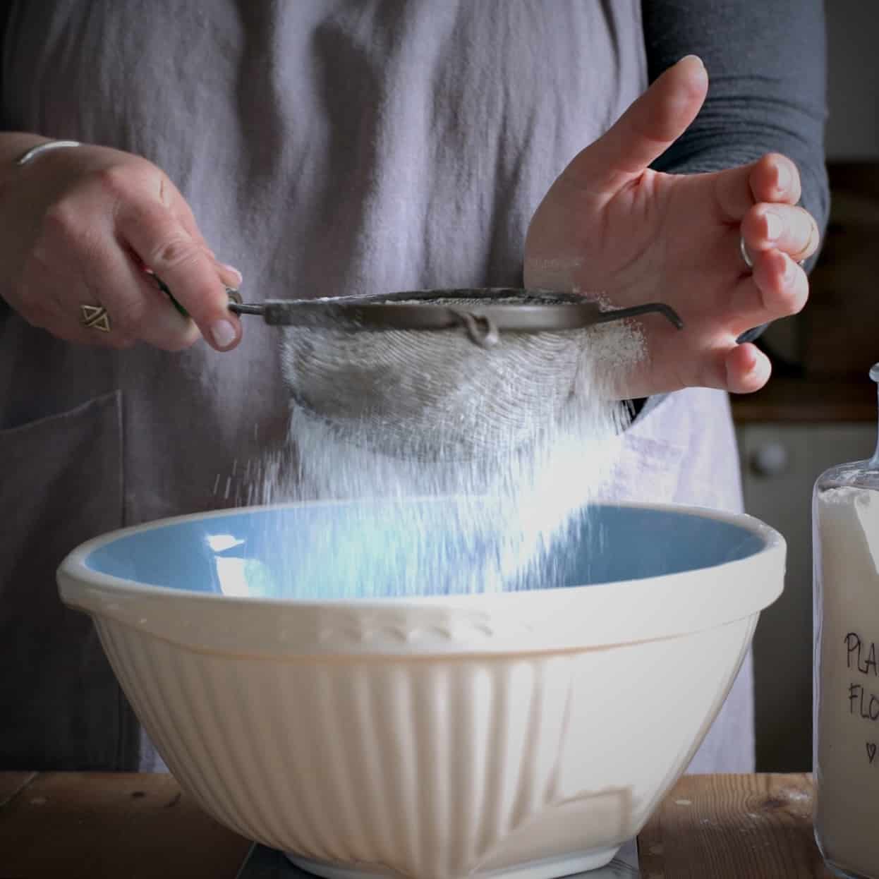 Woman sieving flour in an old fashioned sieve over a blue and white mixing bowl