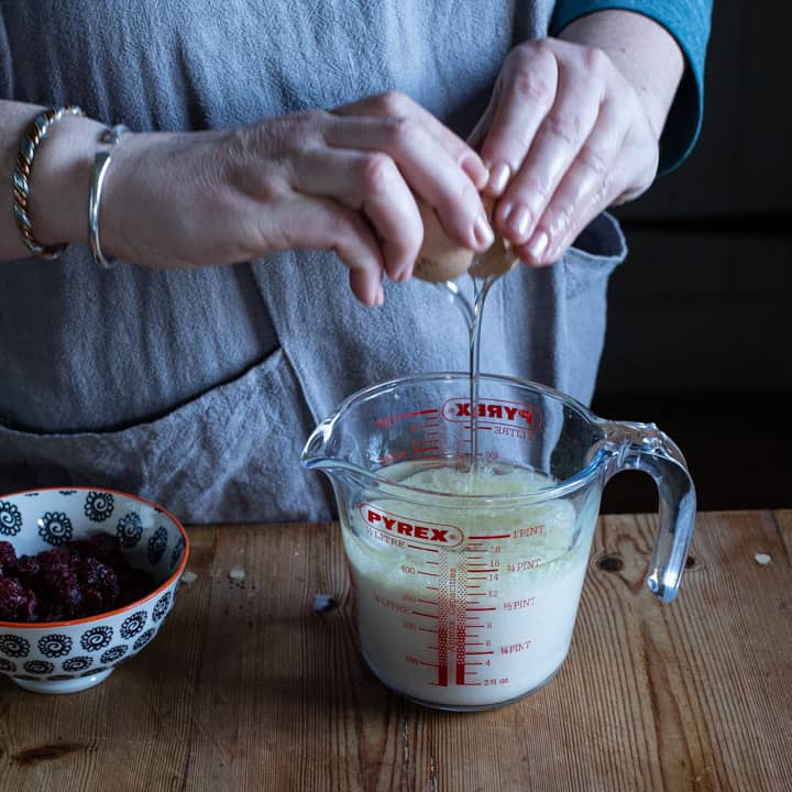 womans hands cracking an egg into a glass jug containing milk and oil ready to make muffins