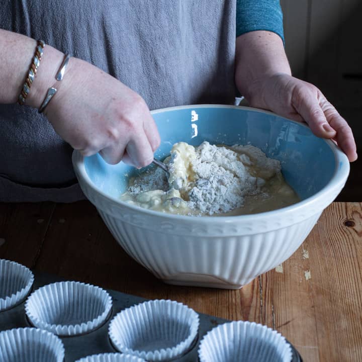 womans hands stirring muffin ingredients inside a big blue and white bowl