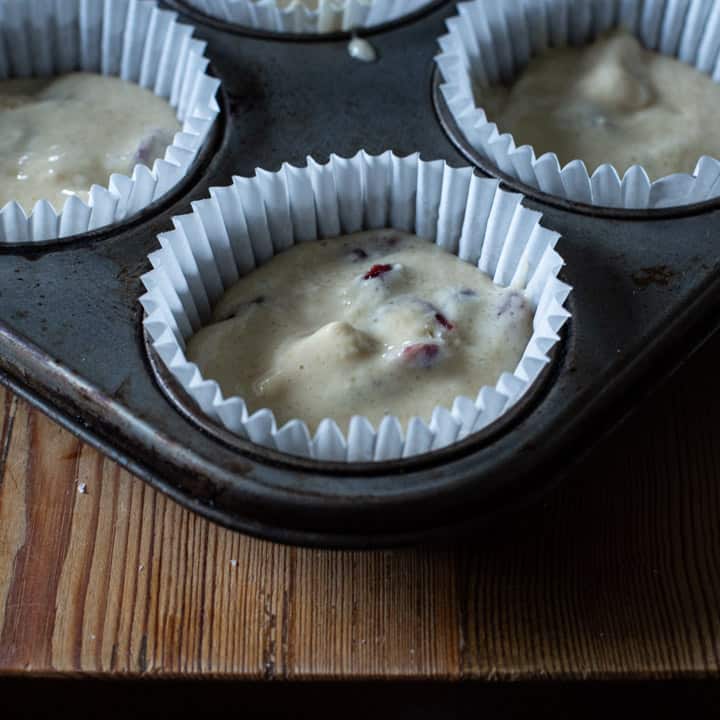 close up of raw muffin batter in a white paper muffin case, inside a metal baking tin