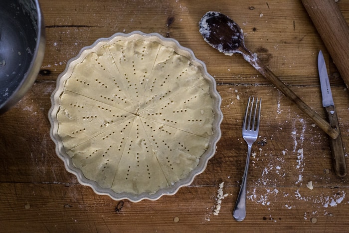 Messy baking scene of wooden background, flan dish with shortbread ready to g in to the oven