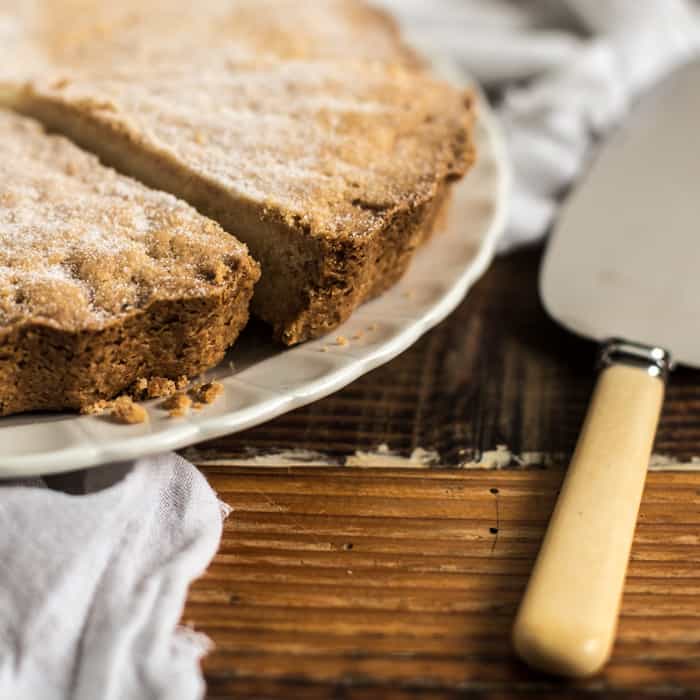 Wooden background with white plate and cake slice, and a close up of the edge of a piece of crumbly shortbread 