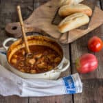 wooden backgrouns with white pan of chicken stew with chorizo and chickpeas