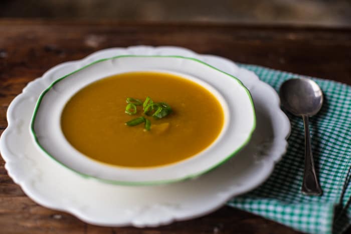 Leek and Butternut Squash Soup in a white bowl with a soup spoon and a green and white check cloth