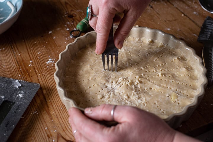 womans hands piercing shortbread in a flan dish with a fork