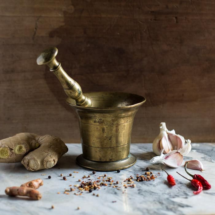 Hot Prawn Madras Curry -brass pestle and morter for grinding spices on a marble slab with ginger root and garlic