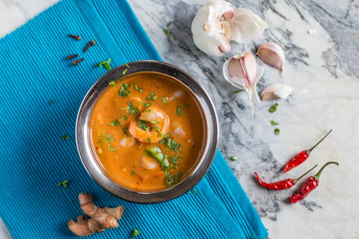 Hot Prawn Madras Curry in a serving bowl on a blue cloth with prawns and chillis