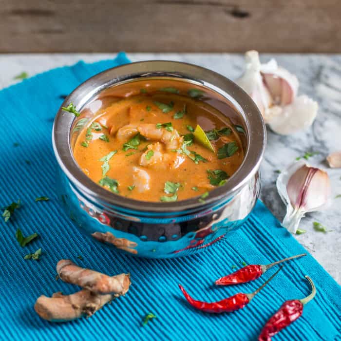 Hot Prawn Madras Curry in a metal bowl with ginger root and red chillis on a blue cloth