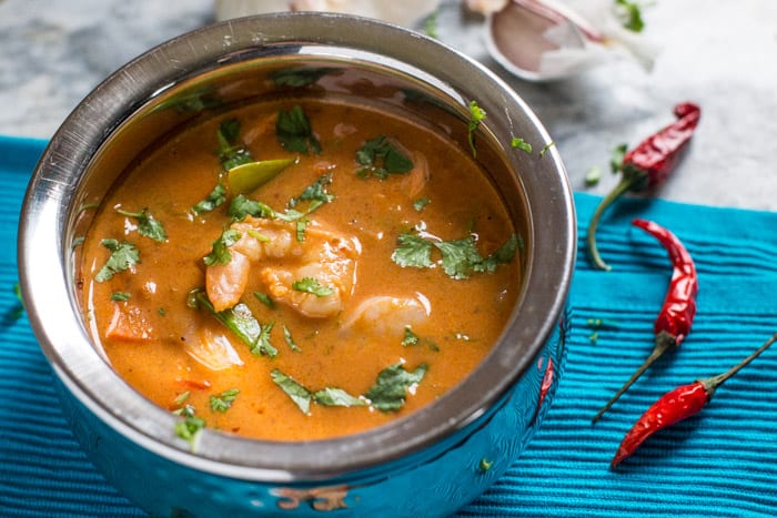 Hot Prawn Madras Curry in a metal bowl with red chillis on a blue cloth