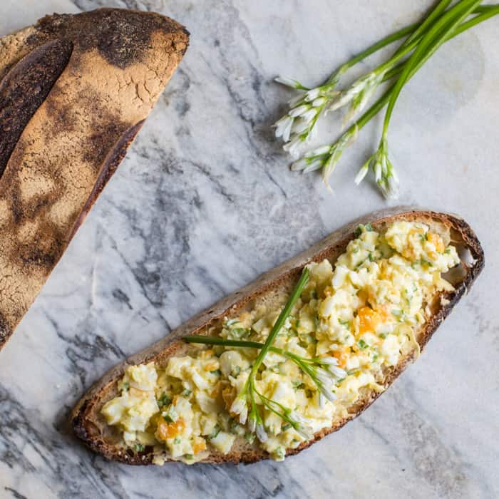 wild garlic egg mayo piled on crusty bread on a marble slab with wild garlic flowers