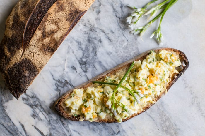 wild garlic egg mayo piled on crusty bread on a marble slab with wild garlic flowers