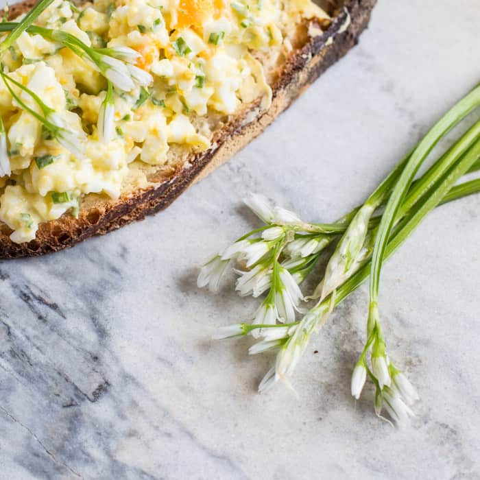 wild garlic egg mayo piled on crusty bread on a marble slab with wild garlic flowers