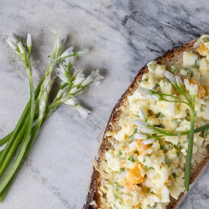 wild garlic egg mayo piled on crusty bread on a marble slab with wild garlic flowers