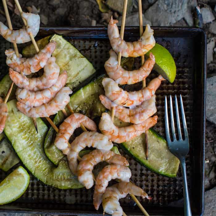 Metal baking tray with kebabs with bright pink prawns and grilled ribbons of courgette