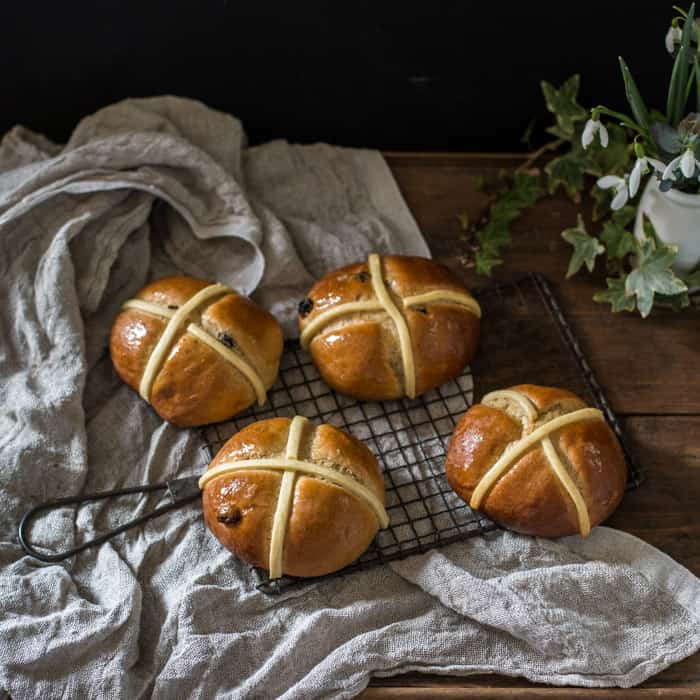 Dairy Free Hot Cross Buns on a cooling tray on a whitecloth with a vase of snowdrops