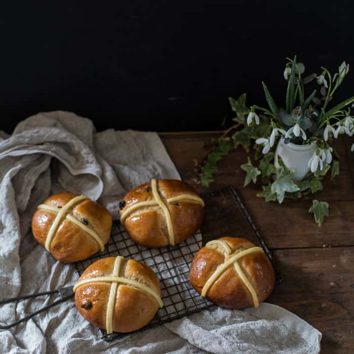 Dairy Free Hot Cross Buns on a cooling tray on a whitecloth with a vase of snowdrops