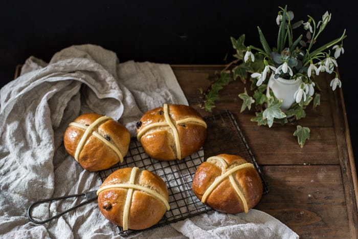 Dairy Free Hot Cross Buns on a cooling tray on a whitecloth with a vase of snowdrops