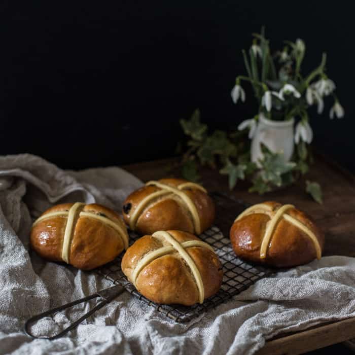 Dairy Free Hot Cross Buns on a cooling tray on a whitecloth with a vase of snowdrops