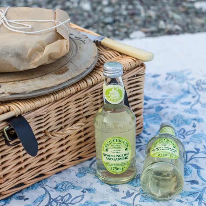 Pressed Picnic Sandwich on a bread board on top of a picnic basket with bottles of Fentimans beside 