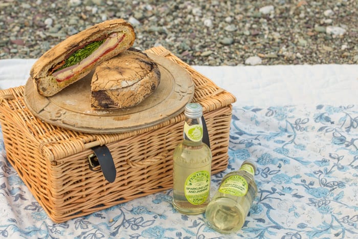 Pressed Picnic Sandwich on a bread board on top of a picnic basket with bottles of Fentimans beside 
