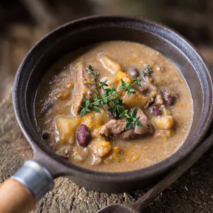 Slow Cooker Pepperpot Stew in a pan on a piece of wood with a serving spoon