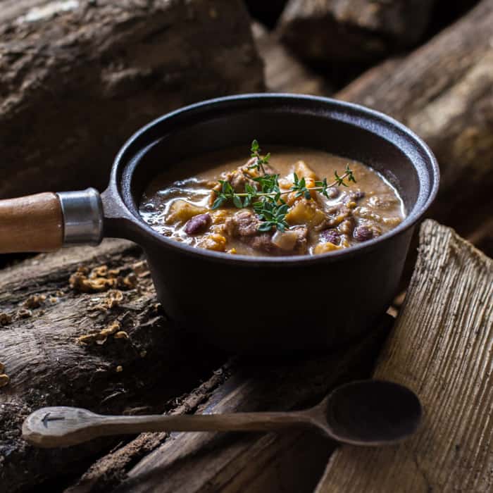 Slow Cooker Pepperpot Stew in a pan on a piece of wood with a serving spoon