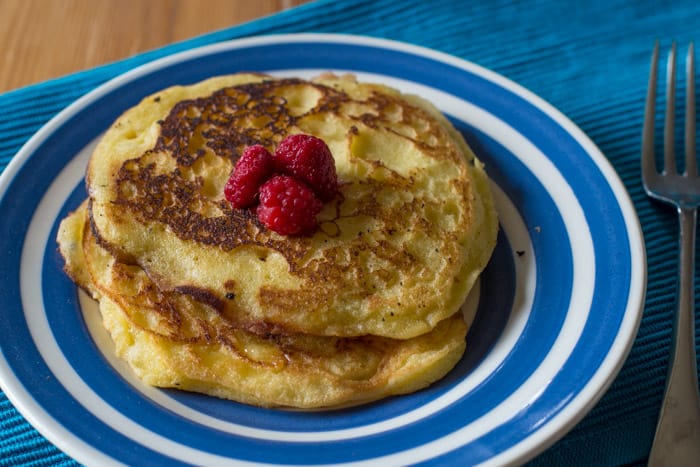 Gluten free camping breakfast -Vanilla Puffy Pancakes topped with Raspberries on a blue and white plate