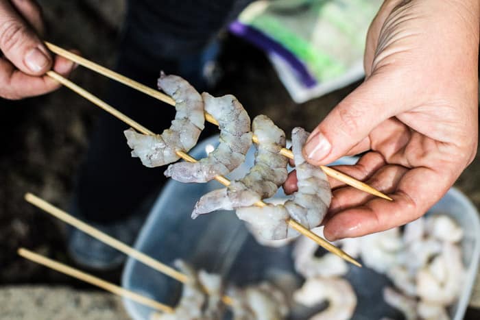 Woman’s hands threading large King prawns onto wooden skewers